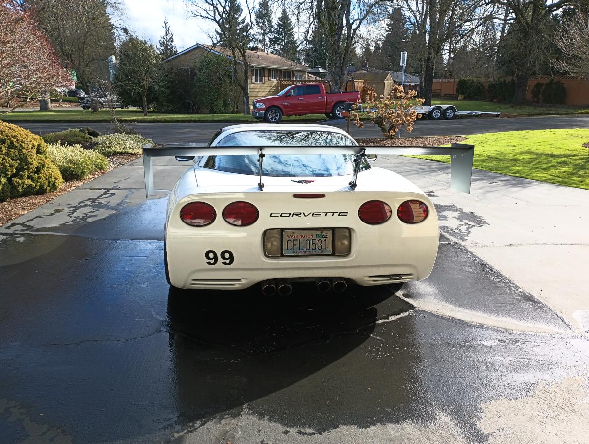 White C5 Chevy Corvette parked in a driveway, taken from the rear of the car, prominently feature the shred Jesse DIY chassis mounted wing powder coated in black
