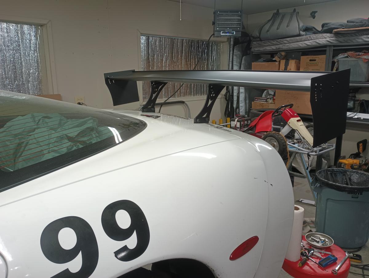A white C5 corvette in a shop with the fully assembled DIY C5 chassis Mounted wing attached to the car.