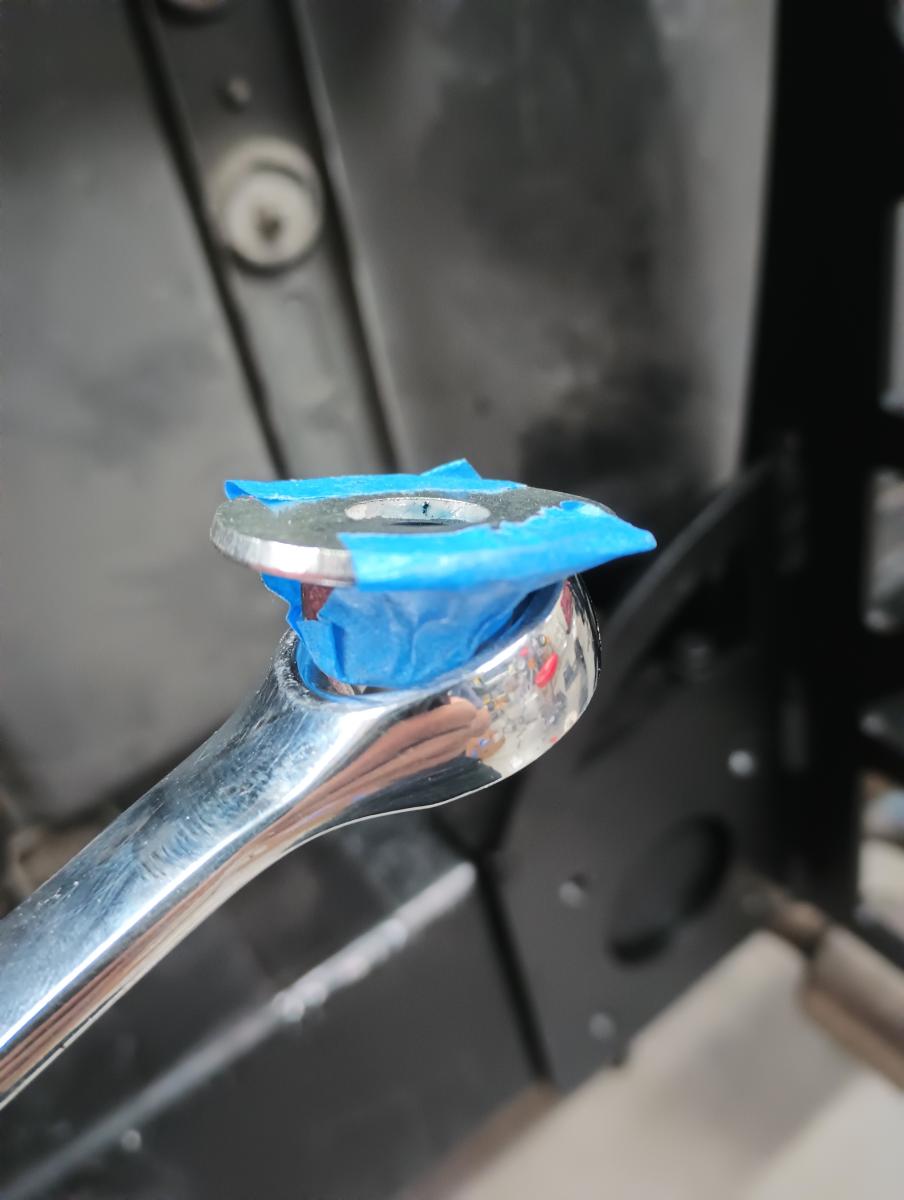 A box wrench with a nut painters taped to a fender washer to help make installation of the chassis mount easier.