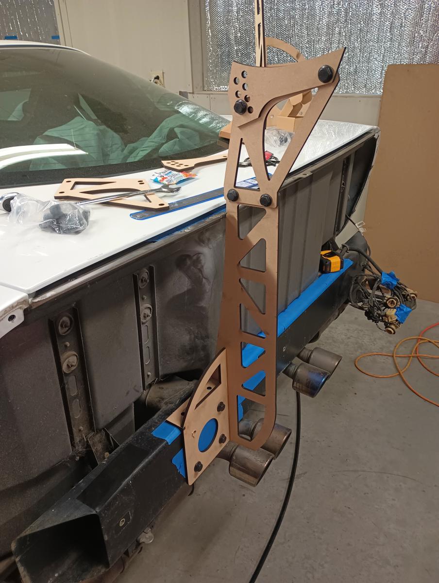 A picture meant to exemplify the chassis mounts attached to the rear bumper 22" from center over blue painters tape. The picture was taken during prototyping so the parts are in MDF instead of powder coated black aluminum.