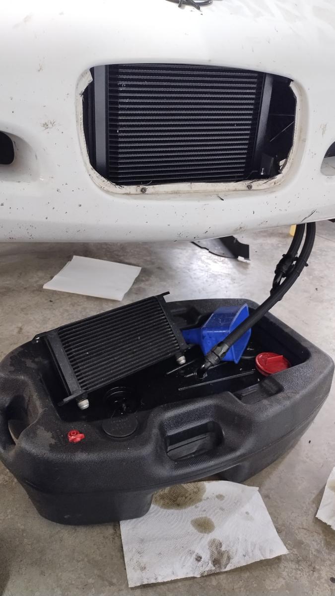 A vertical picture showing the 25 row oil cooler on the Corvette with the bumper on, with the 19 row oil cooler sitting in an oil catch pan below the 1999 C5 Corvette