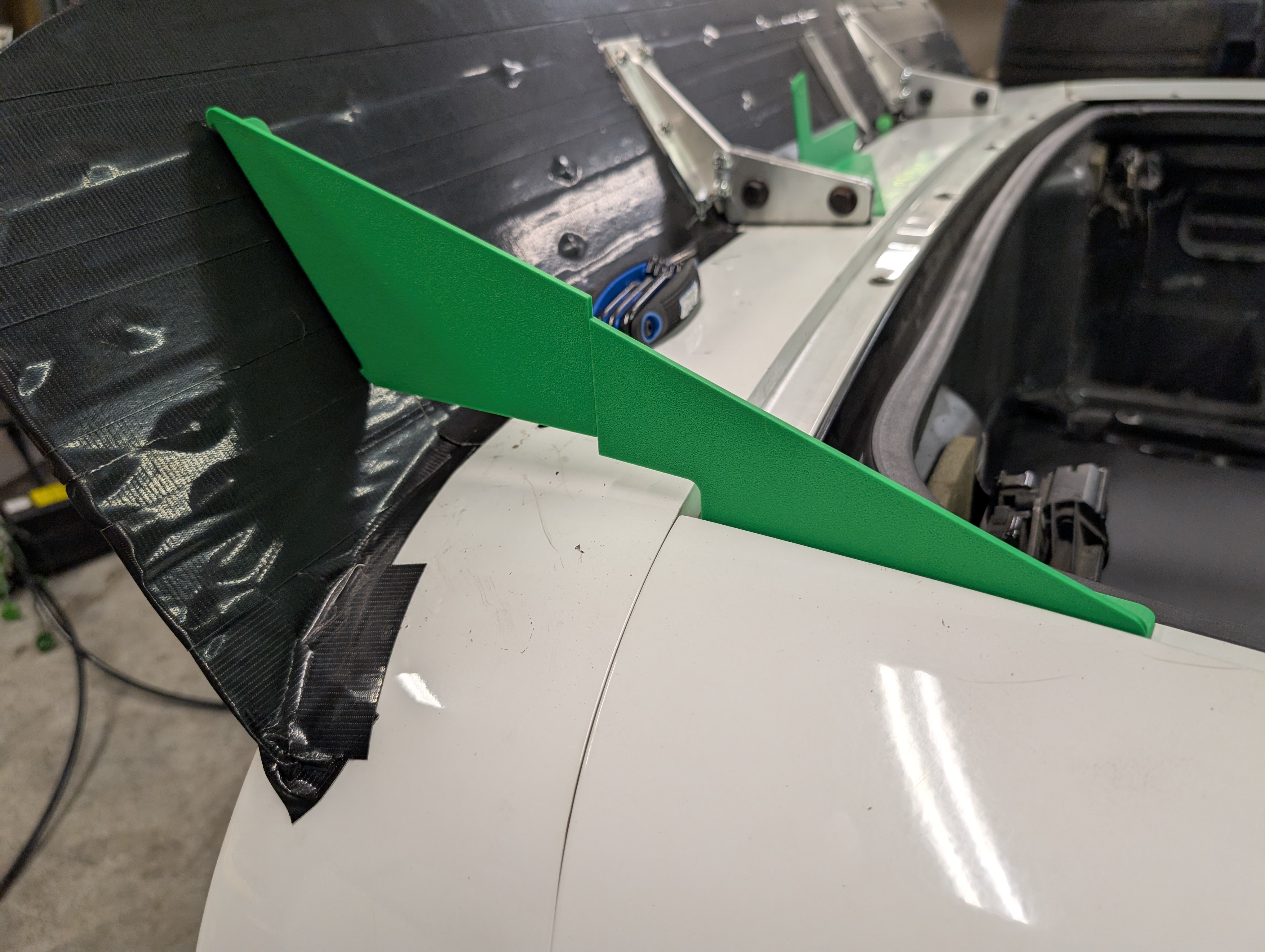 Bright green 3d print test pieces for attaching side of spoiler to beneath the rear of the hatch on a c5 corvette. The brackets are printed in two pieces, and don't align perfectly demonstrating a need for further measurements.