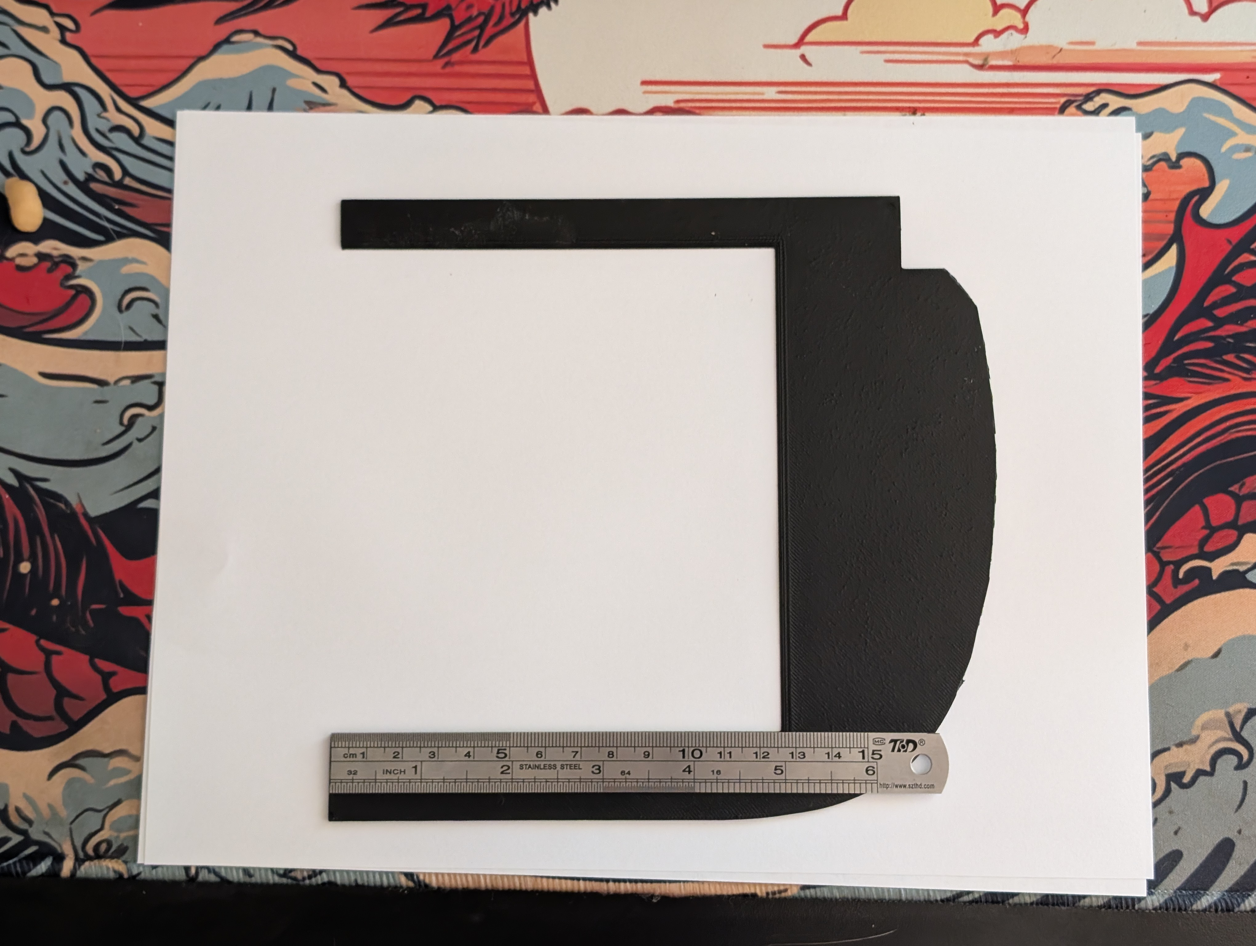 A piece of white paper with a flat printed piece of plastic representing half of the opening of the license plate cover where Shred Jesse runs his DIY oil cooler on his C5 corvette.