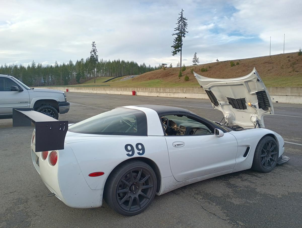 A picture of a white 1999 Targa Top C5 Corvette with the black powder coated chassis mounted wing, parked at The Ridge Motorosports Park for a track day