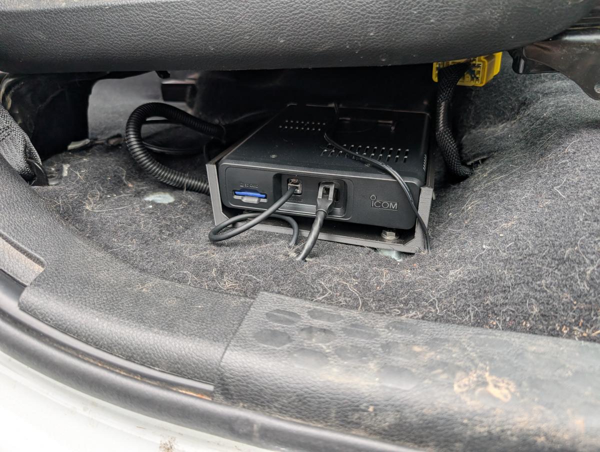 An ICOM-5100 mounted to a 3d printed frame all wired up and plugged in beneath the passenger seat of a ram 3500