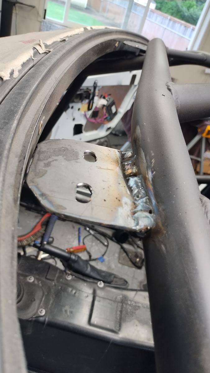 A custom tab for holding the Targa top of a C5 corvette welded to the front windshield support cross bar of the Trackspec rollcage
